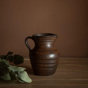 Può includere: Una tazza di ceramica bianca con manico nero e la scritta "But First, Coffee" in nero, in grassetto. La tazza è su una superficie bianca.