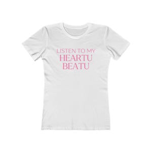 Op de afbeelding: Een wit t-shirt met korte mouwen en de tekst "LISTEN TO MY HEARTU BEATU" in een lichtroze lettertype op de borst gedrukt. Het kledingstuk heeft een ronde hals en een standaard pasvorm, wat zorgt voor een strak en eenvoudig ontwerp.