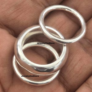 Pode incluir: Três anéis de prata polida com um design de banda lisa e arredondada. Os anéis variam em espessura, com uma banda mais fina e duas bandas mais largas e grossas. O texto JewelryCmStore é visível na superfície dos anéis de prata.