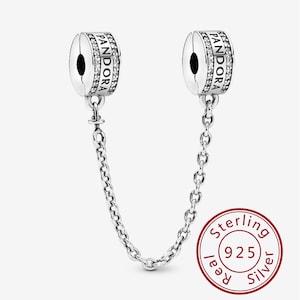 Puede incluir: Un par de clips de encanto Pandora plateados conectados por una cadena. Cada clip presenta el logotipo de Pandora y está adornado con pequeñas piedras transparentes. Un círculo rojo con el texto "Sterling 925 Silver" es visible.