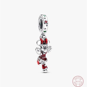 Może przedstawiać: Srebrny charms przedstawiający Minnie Mouse w czerwonej sukience z brokatowymi akcentami, pasującą kokardą i butami. Charms ma pętlę z nazwą marki i wygrawerowanymi słowami "S925 ALE". Biżuteria z motywem Disneya.