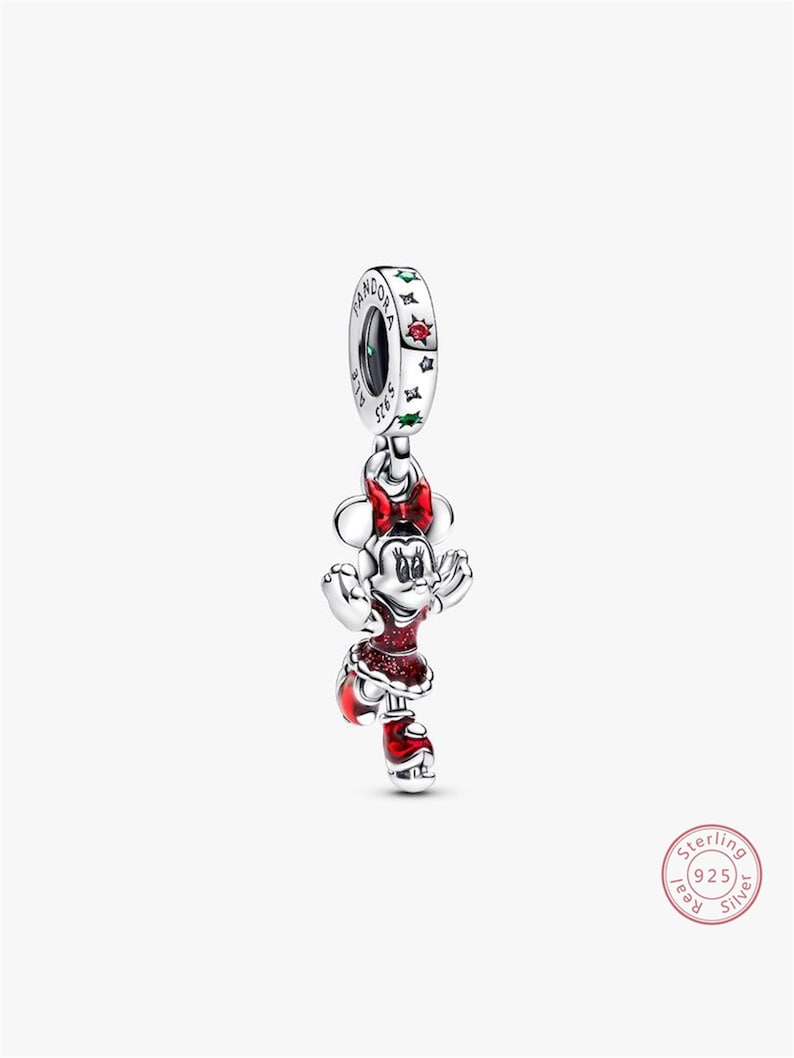 Może przedstawiać: Srebrny charms przedstawiający Minnie Mouse w czerwonej sukience z brokatowymi akcentami, pasującą kokardą i butami. Charms ma pętlę z nazwą marki i wygrawerowanymi słowami "S925 ALE". Biżuteria z motywem Disneya.