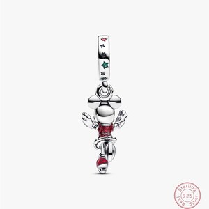 Może przedstawiać: Srebrny charms przedstawiający Minnie Mouse. Charms ma czerwoną sukienkę i buty, z opaską ozdobioną gwiazdami. Ten element biżuterii jest w stylu Disneya, idealny do bransoletki lub naszyjnika.