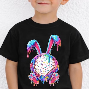 May include: A black t-shirt featuring a colorful graphic of a baseball designed as a bunny. The bunny has blue, pink, and yellow dripping paint. The shirt is worn by a young child wearing sunglasses.