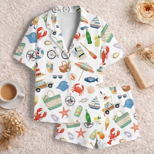 May include: White pajama set with a nautical theme. The short-sleeved top and shorts feature a pattern of beach-related illustrations, including lobsters, sailboats, and sunglasses. The set is made of a soft, lightweight fabric.