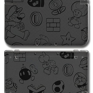 May include: A black Nintendo 3DS handheld game console with a repeating pattern of Mario characters and icons. The design includes Mario, coins, stars, and other elements from the Super Mario video game series. The console is shown open, displaying both screens.