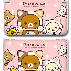 May include: Pink Nintendo 3DS case featuring Rilakkuma characters in bear and cat costumes. The case has the text "Rilakkuma It's a time to relax with cute cats." and paw prints.