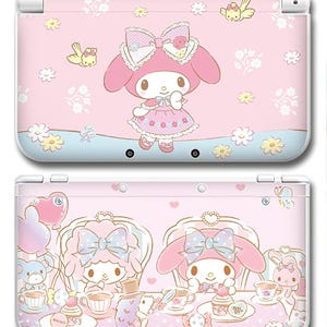 Puede incluir: Consola Nintendo 3DS rosa con un personaje de dibujos animados con un gran lazo y detalles florales. La parte superior de la consola tiene el personaje sobre una línea ondulada azul y blanca. La parte inferior muestra una escena de fiesta de té.