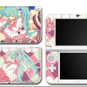 Puede incluir: Consola Nintendo 3DS blanca con un diseño personalizado que presenta una ilustración de estilo anime de una niña con largo cabello turquesa, vestida con un atuendo rosa y blanco. El diseño incluye un patrón de cuadros rosas y blancos y personajes de dibujos animados.