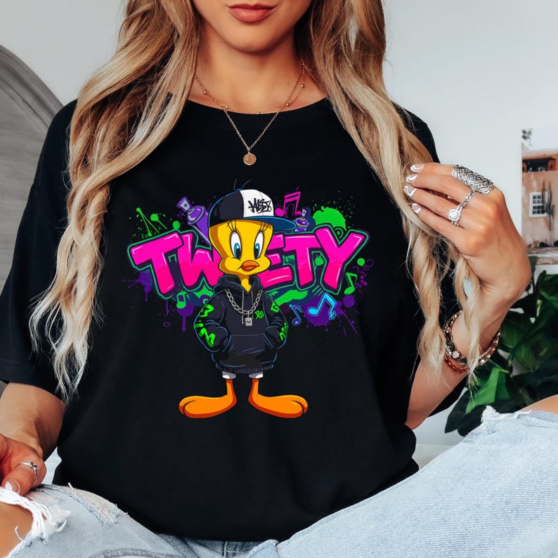 May include: Black t-shirt featuring a cartoon Tweety Bird character wearing a backwards cap and a hoodie with a silver chain. The word "TWEETY" is in pink and green graffiti-style lettering, with musical notes in the background.