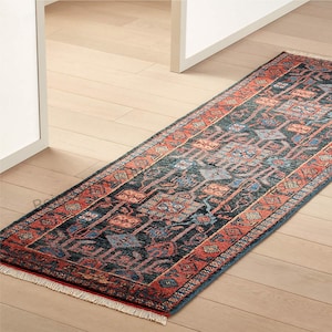 Puede incluir: Una alfombra larga y rectangular con un patrón geométrico detallado. La alfombra presenta un campo central azul oscuro con detalles en rojo, naranja y azul. Los bordes están bordeados con un diseño rojo y naranja. La alfombra tiene un borde con flecos.