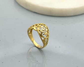 May include: A gold-colored ring with an openwork design. The ring features an intricate pattern of swirling shapes, creating a delicate and ornate appearance. The ring is set against a light gray surface.