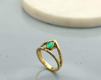 Op de afbeelding: Een goudkleurige ring met een druppelvormige groene edelsteen. De ring heeft een open ontwerp met decoratieve gestippelde details langs de band. De edelsteen is gezet in een V-vormig frame.