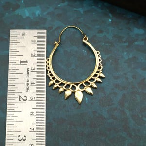 Puede incluir: Pendiente de aro dorado con un diseño decorativo de hojas. El pendiente tiene aproximadamente 5 cm de diámetro. El pendiente tiene un cierre de gancho y está hecho en India.