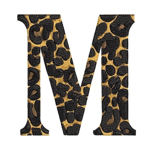 以下が含まれることがあります： ヒョウ柄の刺繍文字「M」。文字は黒色で、ゴールドのアクセントが施され、大胆でスタイリッシュなデザインになっています。画像は白い背景にあります。