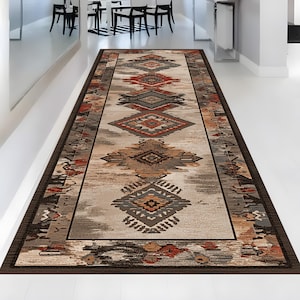 May include: A rectangular runner rug with an intricate geometric pattern in shades of brown, beige, gray, and rust. The rug features a dark brown border and a central design of diamond and tribal motifs. The rug is placed on a white floor.