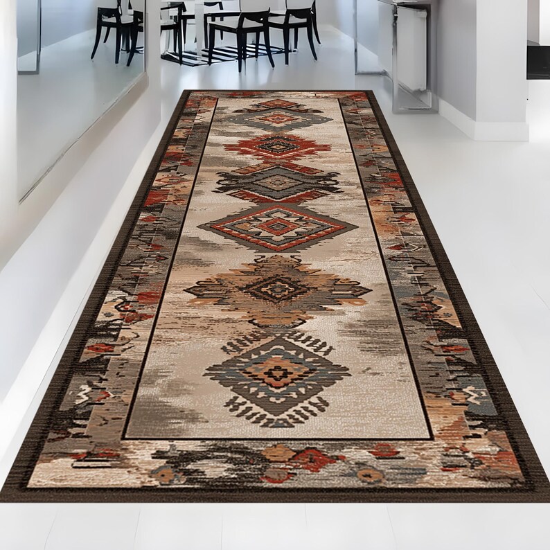 May include: A rectangular runner rug with an intricate geometric pattern in shades of brown, beige, gray, and rust. The rug features a dark brown border and a central design of diamond and tribal motifs. The rug is placed on a white floor.