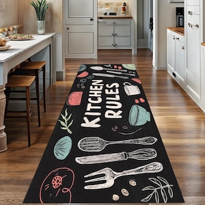 May include: Black rectangular kitchen runner rug with white text that reads "KITCHEN RULES". The rug features illustrated kitchen utensils and food items in white, teal, pink, and green.