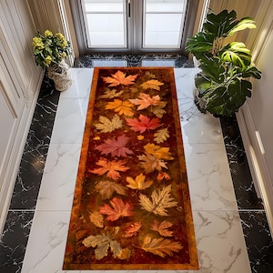 Puede incluir: Una alfombra rectangular con un diseño de hojas de otoño en tonos rojos, naranjas y amarillos. La alfombra tiene un fondo marrón oscuro y un borde a juego. La alfombra está colocada sobre un suelo de baldosas blancas y negras.