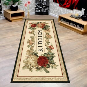 May include: A rectangular kitchen rug with a cream-colored background, featuring a floral design with red and cream roses, green leaves, and the word "KITCHEN" in black. The rug has a dark green border with a decorative trim.