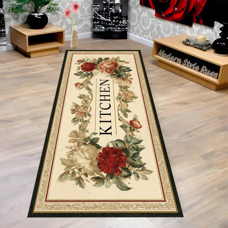 May include: A rectangular kitchen rug with a cream-colored background, featuring a floral design with red and cream roses, green leaves, and the word "KITCHEN" in black. The rug has a dark green border with a decorative trim.