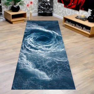 Puede incluir: Una alfombra rectangular con un diseño de remolino oceánico en tonos azules y blancos. La obra de arte representa un vórtice de agua, creando un efecto visual dramático y dinámico. La alfombra está diseñada para ser colocada sobre un suelo de madera.