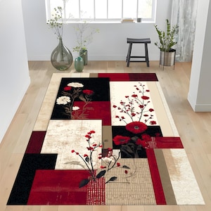 May include: A rectangular area rug with a floral design. The rug features a geometric pattern with squares of black, red, and beige. White and red flowers are depicted throughout the design. The rug is placed on a wooden floor.