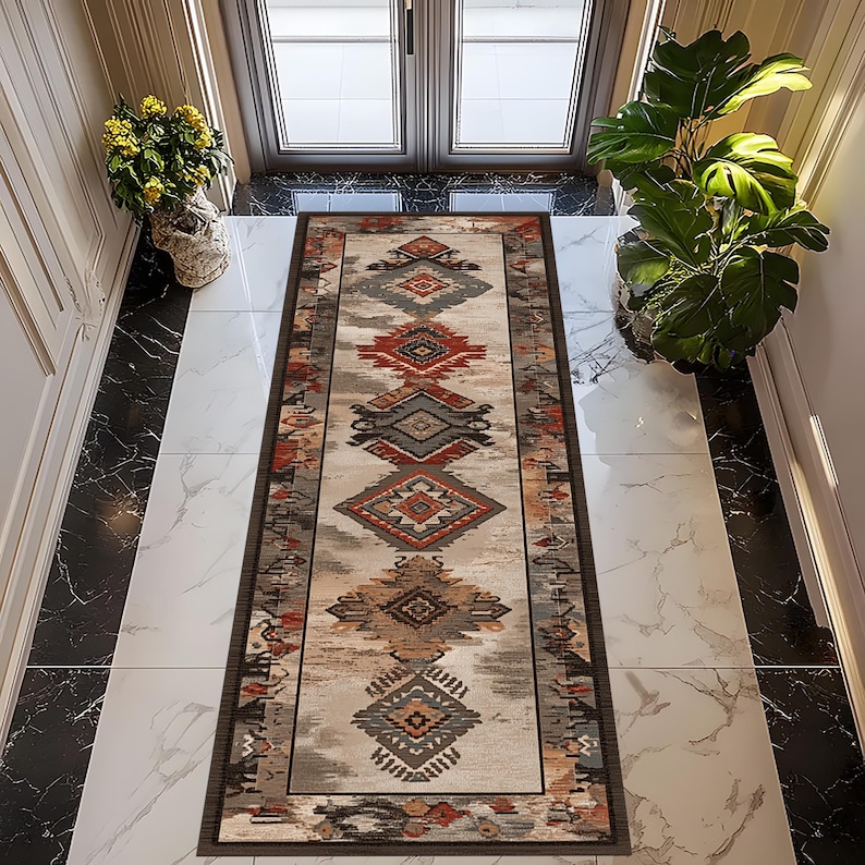 May include: A rectangular, patterned rug with a beige background and geometric designs in shades of red, gray, and brown. The rug has a dark brown border and is placed in a hallway with marble flooring.