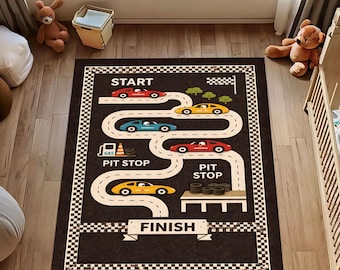 Puede incluir: Una alfombra rectangular negra con un diseño de pista de carreras. La pista presenta coches de carreras de colores, una línea de salida y llegada, y paradas en boxes. El borde tiene un patrón de cuadros.