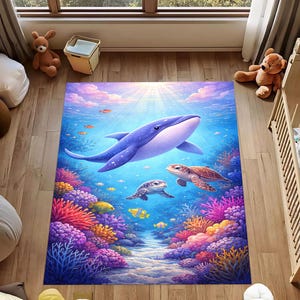 Op de afbeelding: Een levendig vloerkleed met een onderwaterlandschap met een grote blauwe walvis, twee zeeschildpadden en kleurrijke koraalriffen. Het kleed heeft een blauwe achtergrond met vissen en zonnestralen, wat een grillige en uitnodigende sfeer creëert.
