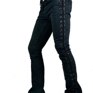 Puede incluir: Vaqueros de mezclilla de lavado oscuro con detalles de cordones en las costuras exteriores. Los vaqueros tienen un ligero acampanado en la parte inferior y se combinan con botas negras. El estilo es atrevido y alternativo.