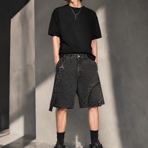 Op de afbeelding: Een persoon draagt een zwart t-shirt, zwarte denim shorts met bandjes, zwarte sokken en zwarte platform sneakers. De outfit heeft een grunge- of streetwear-esthetiek.
