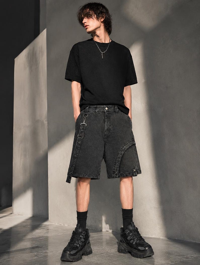Op de afbeelding: Een persoon draagt een zwart t-shirt, zwarte denim shorts met bandjes, zwarte sokken en zwarte platform sneakers. De outfit heeft een grunge- of streetwear-esthetiek.
