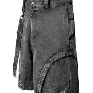 Op de afbeelding: Zwarte denim shorts met een distressed, acid-wash afwerking. De shorts hebben een uniek ontwerp met een band en metalen vetergaten. De shorts hebben een knoop- en ritssluiting en zakken.