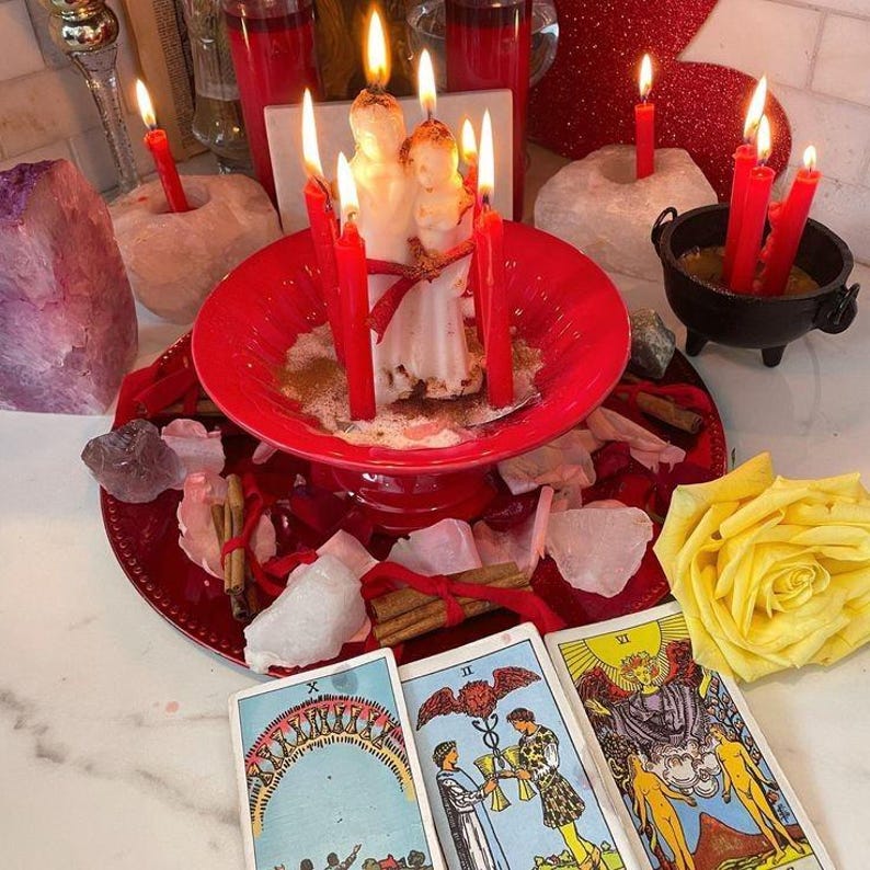 Puede incluir: Una disposici&oacute;n espiritual con velas rojas encendidas, una vela blanca central y cartas del tarot. La escena incluye un plato rojo, cristales, palitos de canela y una rosa amarilla, creando un ambiente m&iacute;stico.