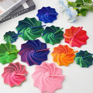 May include: A collection of colorful, star-shaped objects with a spiral design, each with a stick in the center. Colors include pink, red, orange, yellow, green, and blue. A book with the text "YOU CAN Love and Love" is also visible.