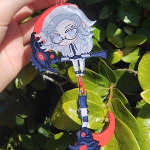 May include: Anime-style keychain in red, white, and black, depicting a character with gray hair, glasses, and a white outfit. The keychain has a red clasp and a blue and red scythe charm attached.