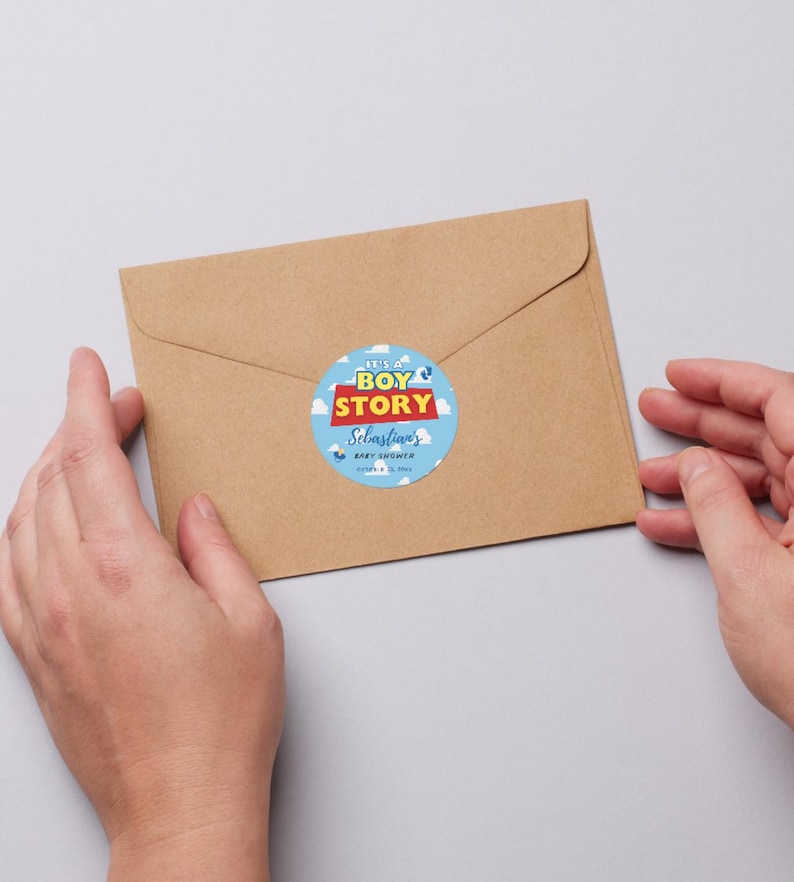 May include: A brown envelope with a round sticker that reads "It's a Boy Story" in blue, red, and white. The sticker is for Sebastian's baby shower. The envelope is held by two hands.