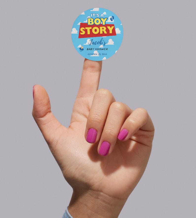 May include: A round baby shower sticker with the text "It's a Boy Story" in blue, red, and yellow. The sticker includes the name "Jacob's" and the date "October 23, 20xx" on a light blue background with clouds.