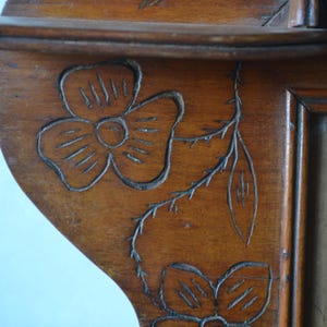 May include: Close-up of a wooden shelf with carved floral designs. The shelf is made of a warm-toned wood and features two carved flowers and a stem with leaves. The shelf has a scalloped edge.