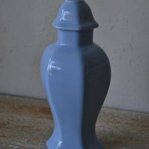Może przedstawiać: Jasnoniebieski ceramiczny wazon o unikalnym, geometrycznym kształcie. Wazon ma rozszerzoną podstawę, zaokrąglony korpus i pokrywę. Wazon ma około 25 cm wysokości.