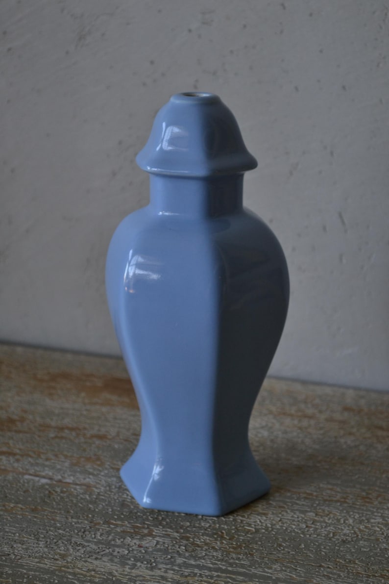 Może przedstawiać: Jasnoniebieski ceramiczny wazon o unikalnym, geometrycznym kształcie. Wazon ma rozszerzoną podstawę, zaokrąglony korpus i pokrywę. Wazon ma około 25 cm wysokości.