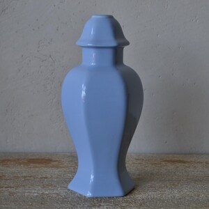 Może przedstawiać: Jasnoniebieski ceramiczny wazon o geometrycznym kształcie. Wazon ma sześciokątną podstawę i pasującą pokrywkę. Wazon ma około 30 cm wysokości.