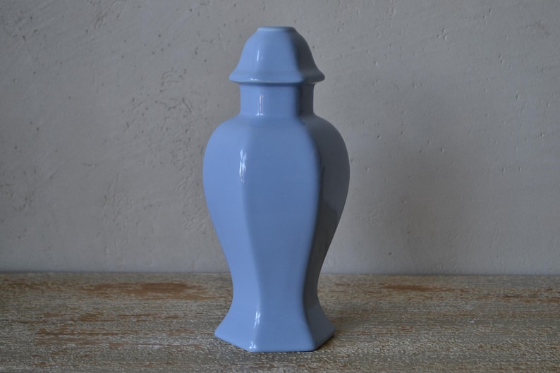 Może przedstawiać: Jasnoniebieski ceramiczny wazon o geometrycznym kształcie. Wazon ma sześciokątną podstawę i pasującą pokrywkę. Wazon ma około 30 cm wysokości.
