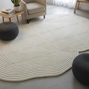 Puede incluir: Alfombra de área texturizada de color blanquecino con un diseño único y fluido. La alfombra presenta patrones concéntricos en forma de onda. Dos pufs de punto gris oscuro se colocan cerca de la alfombra. La alfombra es una adición suave y neutra a cualquier espacio habitable.