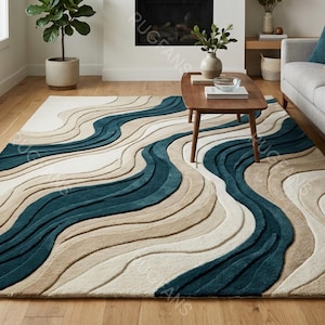 Op de afbeelding: Een rechthoekig vloerkleed met een golvend patroon. Het kleed heeft afwisselende banden in teal, beige en gebroken wit. Het ligt op een houten vloer in een woonkamer. Het ontwerp lijkt op een rivier.