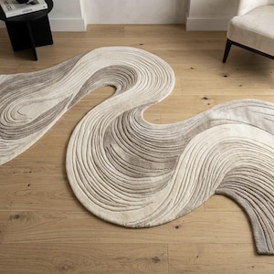 Puede incluir: Dos alfombras abstractas en forma de ola, en tonos neutros de beige y gris. Las alfombras presentan un patrón texturizado y arremolinado, colocadas sobre un suelo de madera clara. El diseño añade un toque moderno a la decoración de la habitación.