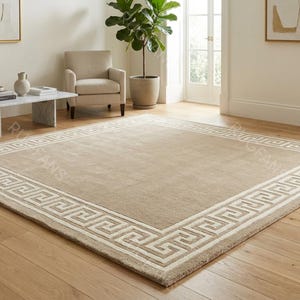 Puede incluir: Una alfombra rectangular beige con un borde de diseño de greca. La alfombra está centrada en un suelo de madera en una habitación bien iluminada. El borde es de un tono beige más claro.