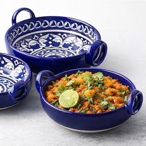 May include: Three blue ceramic serving bowls with white floral patterns. One bowl contains a dish with a lime garnish. Each bowl has two handles. The bowls are on a white surface.