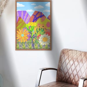 May include: A framed art print featuring a colorful landscape with stylized mountains, flowers, and a blue sky with clouds. The artwork is in a wooden frame and hangs on a white wall near a brown leather chair.